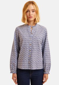 Blusa floreale blu con maniche lunghe, scollatura rotonda e chiusura a bottoni. Presenta un motivo di fiori bianchi e dettagli delle maniche arricciati.