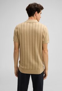 Beige overhemd met korte mouwen, voorzien van een ribbelstructuur en verticale strepen. Het heeft een platte kraag en een iets verlengde zoom.