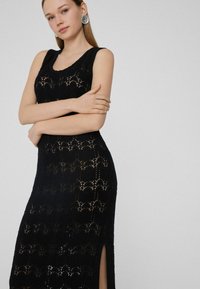 Schwarzes, ärmelloses Strickkleid mit Wellenmuster und seitlichem Schlitz, das ein strukturiertes Design und eine figurbetonte Silhouette aufweist.