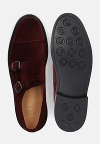 Burgunderfarbene Wildleder-Slip-On-Schuhe mit doppelten Schnallen, schwarzen Gummisohle mit kreisförmigen Mustern und beigem Innenfutter. Minimalistisches Design.