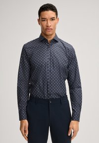 Camicia blu navy con motivi bianchi piccoli, collo con bottoni, maniche lunghe e taglio sagomato, abbinata a pantaloni blu navy.
