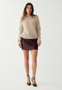 Bézs színű mohair pulóver hosszú ujjakkal, burgundi színű flitteres miniszoknyával párosítva. A modellen fekete, hegyes orrú, bokapántos magassarkúk vannak.