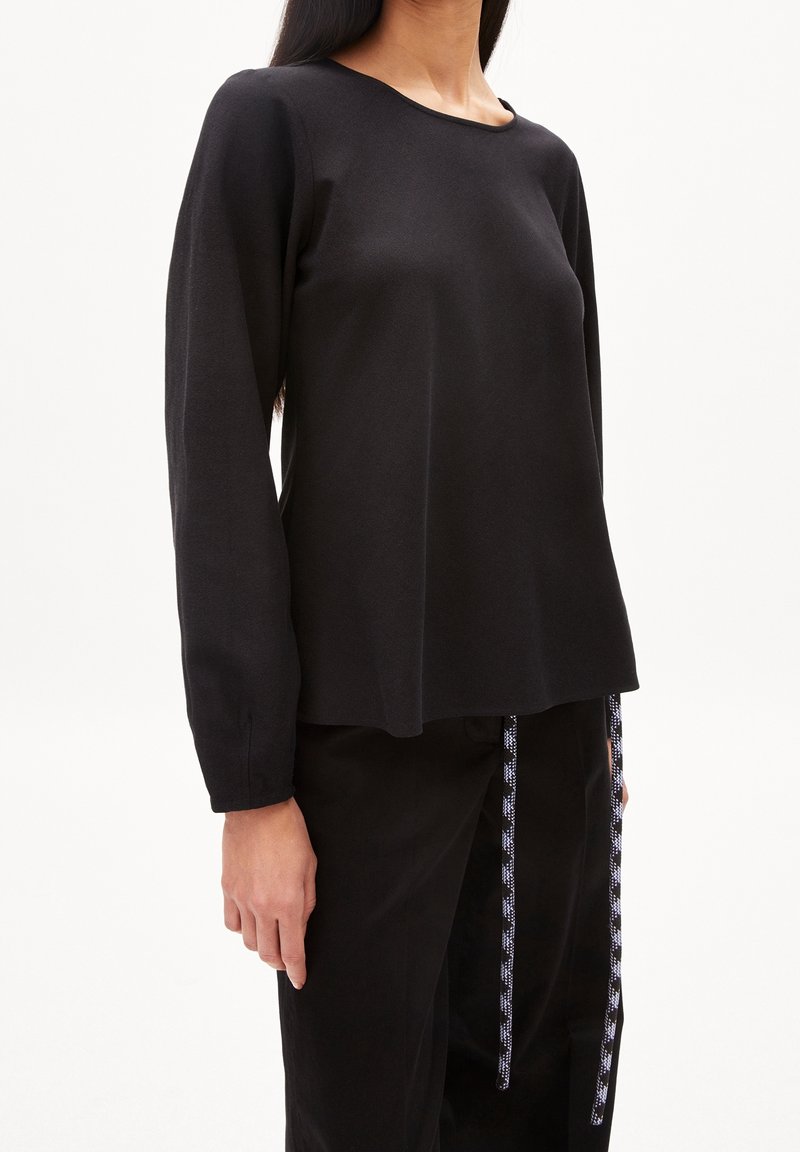 Femme portant un haut noir uni à manches longues associé à un pantalon noir avec des cordons de serrage noirs et blancs à motifs.