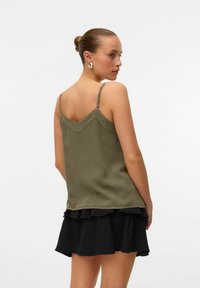 Débardeur vert olive sans manches avec des bretelles ajustables et un dos en V, associé à une jupe noire à volants. Texture de tissu lisse.