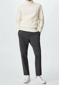 Cremfarbener, gerippter Rollkragenpullover kombiniert mit dunkelgrauen, taillierten Hosen und weißen Sneakern. Weicher Stoff, schlanker Schnitt und klare Linien.