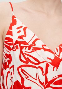 Punase ja valgete värvidega kleit, millel on lillemuster, V-kaeluse disain ja tekstureeritud kangas, millel on vertikaalsed voldikud. Nudistõmblused.