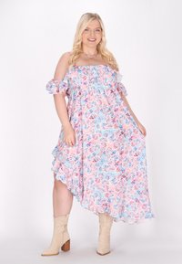 Abito lungo floreale con maniche a spalle scoperte, tonalità pastello di blu e rosa, orlo a volant, abbinato a stivali da cowboy beige.