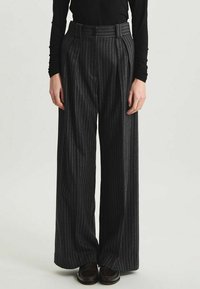 Pantalons à jambes larges gris foncé avec des rayures verticales. Fabriqués à partir d'un tissu texturé, ils présentent une taille haute et des plis.