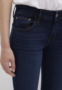 Dark blue denim jeans featuring a high waist, front pockets with contrasting stitching, and a smooth texture. Stitching is visible at seams.