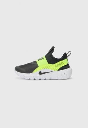Black athletic shoe with a neon green strap, featuring a textured upper, white speckled sole, and a pull tab on the heel.