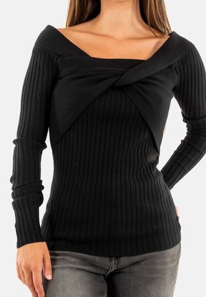 Vrouw draagt een zwart, geribbeld, langarmig topje met een gedraaide off-shoulder halslijn en grijze broek, getoond van schouders tot heupen.