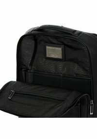 L'interno dello zainetto in pelle nera presenta una tasca con zip e un'etichetta brandizzata. Il tessuto testurizzato aggiunge profondità, completato da cerniere eleganti.