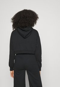 Czarny, krótki hoodie z kapturem na sznurku. Wykonany z miękkiego materiału, o jednolitej kolorystyce oraz ściągaczach na mankietach i u dołu. Prosty design bez wzorów.