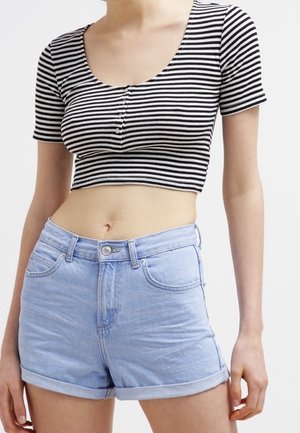 Woman wearing black and white striped short-sleeve crop top and light blue rolled-hem denim shorts against a plain background.
