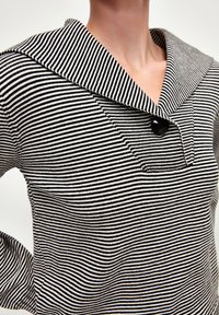 Pull en rayures noir et blanc avec un large col, orné d'un bouton noir unique et d'un tissu texturé. Gros plan sur le col et la zone de la poitrine.