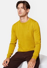 Żółty sweter wykonany z teksturowanej dzianiny, z okrągłym dekoltem i długimi rękawami. Posiada małe haftowane logo na piersi.