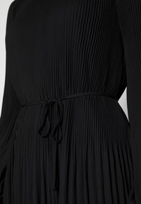 Czarna sukienka z plisowanym wzorem, długimi rękawami i dopasowanym talią z detalem w postaci wiązania. Miękka tekstura i gładkie wykończenie materiału.