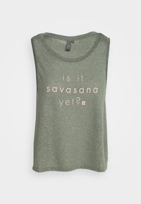 Zelený bezrukávový top s uvolněným střihem. Na přední straně má světle růžový text s nápisem "už je na řadě savasana?". Měkká textilie.