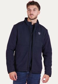 Veste en polaire bleu marine avec fermeture éclair, col haut et logo sur la poitrine gauche. Dispose de deux poches avant et d'un tissu doux et texturé.