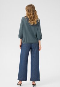 Pull surdimensionné teal à manches trois-quarts associé à un pantalon en jean large taille haute de couleur foncée et des sandales à talons noires.