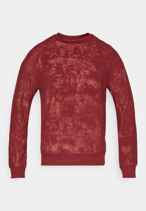 Červený crewneck sveter s textúrovaným povrchom, s dlhými rukávmi a rebrovanými manžetami, ozdobený malým logom na hrudi.