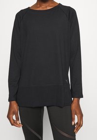 Czarna, długosleeve'owa koszulka sportowa z okrągłym dekoltem, rękawami raglanowymi i luźnym krojem, z dyskretnymi detalami w szwach.