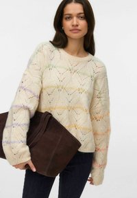 Maglione lavorato a maglia crema chiaro con motivi a onde colorate in tonalità pastello, abbinato a una borsa in camoscio marrone scuro e jeans scuri.