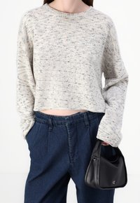 Sweter kremowo-szary w melanżowy wzór, z okrągłym dekoltem i krótkim fasonem, zestawiony z ciemnymi, wysokim stanem spodniami dżinsowymi oraz czarną torebką.