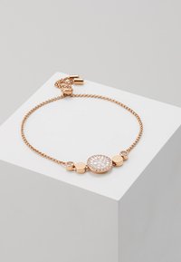 Armbånd i rosagull med kjededesign, en sirkulær midtdel med hvit steininnlegg og sirkulære metalldetaljer. Justerbar lås.