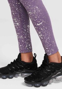 Leggings morados con manchas plateadas, con el logo de Nike, combinados con zapatillas deportivas negras con amortiguación de aire transparente y cordones dinámicos.