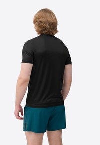 Zwart sportshirt met korte mouwen, gemaakt van een gladde stof, gedragen met teal shorts. Het shirt heeft een getailleerde snit en een eenvoudig ontwerp.