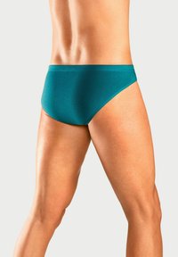 Türkisblaue Badeslips aus glattem Stoff, mit einer niedrigen Taille und minimaler Bedeckung, in einem klaren, schlichten Design.