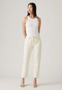 Witte geribbelde tanktop gecombineerd met off-white high-waisted straight-leg jeans, met een rafelige zoom en minimale metalen accenten.