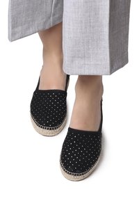 Mustadest sametist espadrillod, millel on metallist kaunistused, jute köitest põhi ja pehme, tekstureeritud ülemine osa. Igapäevane libisev mudel.