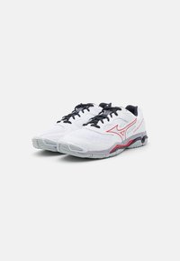 Pair of white athletic shoes with black laces, red logo accents, and gray soles on a plain white background.