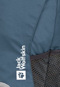 Blauwe stoffen rugzak met een textuurpatroon, een gaas zijvak en een opvallend wit logo. Heeft een slank ontwerp en versterkte stikseldetails.