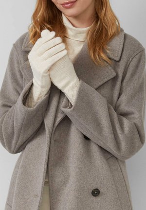 Grauer Wollmantel mit großen Revers; das Model trägt cremefarbene gestrickte Handschuhe, deren strukturierte Bündchen gegen den Mantel sichtbar sind.