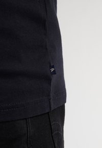 Camiseta de algodón azul marino con una costura lateral que presenta un pequeño logotipo bordado. Textura suave, corte regular y mangas cortas.
