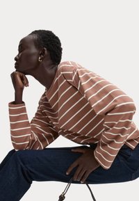 Bruin gestreepte lange mouw shirt met witte strepen, met een losse pasvorm en ronde halslijn, gecombineerd met donkerblauwe denim jeans.