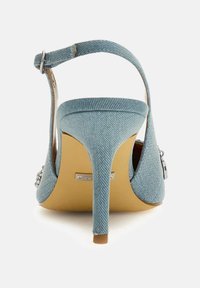 Denim high heel shoe with an ankle strap, pointed toe, and a sleek stiletto heel. Textured blue fabric with a smooth beige sole.