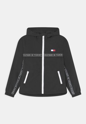 Schwarze Kapuzenjacke mit weißem Frontreißverschluss, Reißverschlusstaschen und Tommy Hilfiger-Branding auf Brust, Ärmeln und quer über der Brust.