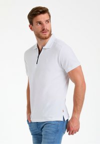 Hvid polo-shirt med struktureret stof, korte ærmer og lynlåsekrave. Har et lille logo på brystet og sidelufter.