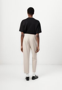 Black short-sleeve shirt paired with high-waisted, light beige trousers. Model wears black shoes and white socks. Simple, minimal design.