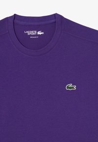 Camiseta de algodón púrpura con cuello redondo y mangas cortas. Destacable logo de cocodrilo en verde y rojo en la parte izquierda del pecho. Corte regular.