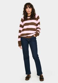 Brun och rosa randig tröja med vid halsringning och ribbade ärmslut, ihop med mörkblå raka jeans och bruna loafers.