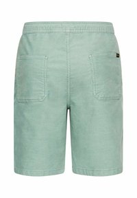 Lichtgroene corduroy shorts met elastische tailleband en twee grote vierkante achterzakken, gezien van achteren op een witte achtergrond.