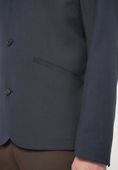 Tengerészkék blézer texturált anyagból, egysoros gombolással és elegáns bevágott gallérral. Rejtett oldalzsebbel és testhezálló szabással.