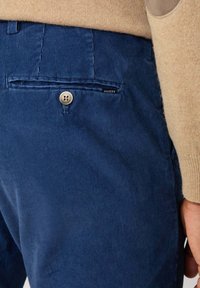 Pantaloni di velluto a coste blu navy con una superficie testurizzata, dotati di una tasca posteriore con chiusura a bottone e un piccolo'etichetta 'Hackett'.