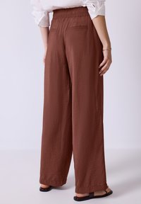Bruine, wijde broek met een elastische tailleband en zachte, gestructureerde stof. Bevat twee achterzakken en heeft een lichte uitvoering.