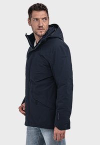 Marineblaue wasserdichte Jacke mit Kapuze, Reißverschlusstaschen und durchgehendem Reißverschluss. Verfügt über eine strukturierte Oberfläche mit minimalem Branding.